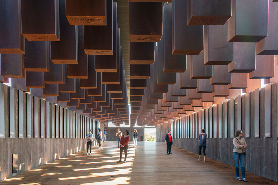 Multiple people standing inside the National Memorial for Peace and Justice, observing the Corten steel monuments—one for each county where a racial terror lynching took place.