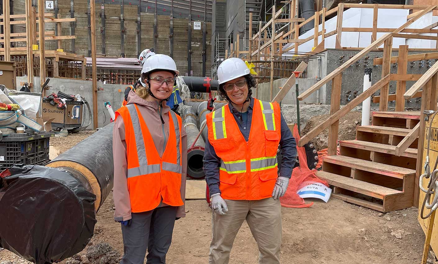 Two women dressed in construction PPE stand at a construction site